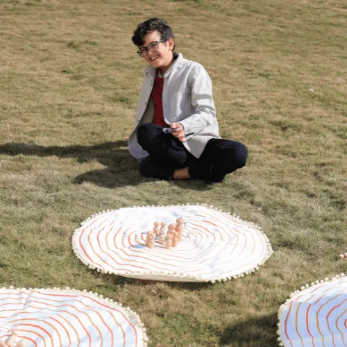 A boy sitting on the grass next to the Circle of Life mat and its characters