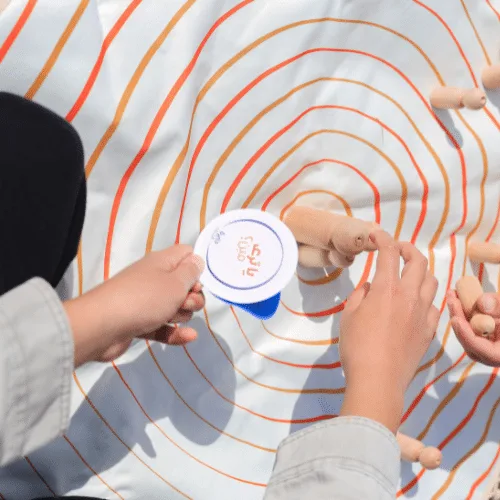A child holding a Circle of Life question card above the circles of the play mat