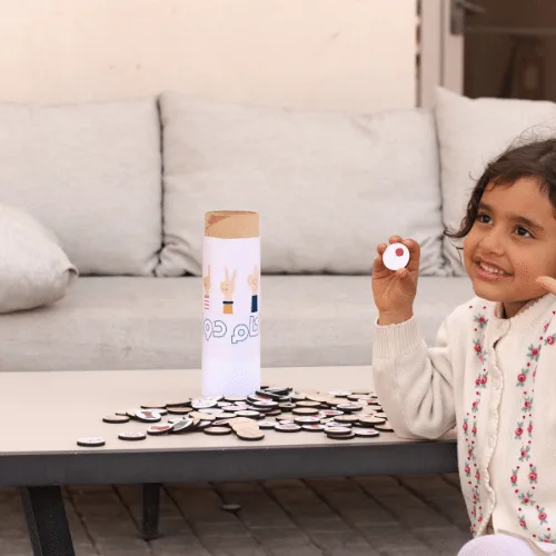A girl sitting at home showing a Kam Dool wooden coin