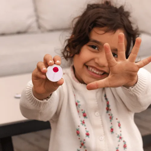 A smiling girl holding up a Kam Dool coin towards the camera