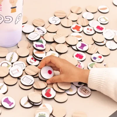 A hand picking up Kam Dool wooden coins printed with everyday products