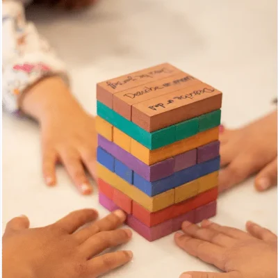 Children's hands around a tower of coloured wooden Like Jenga blocks