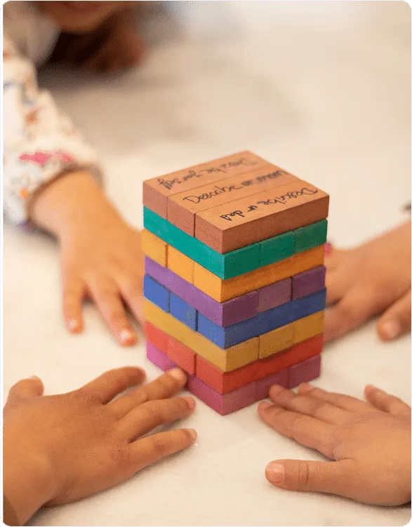 Children's hands around a tower of coloured wooden Like Jenga blocks