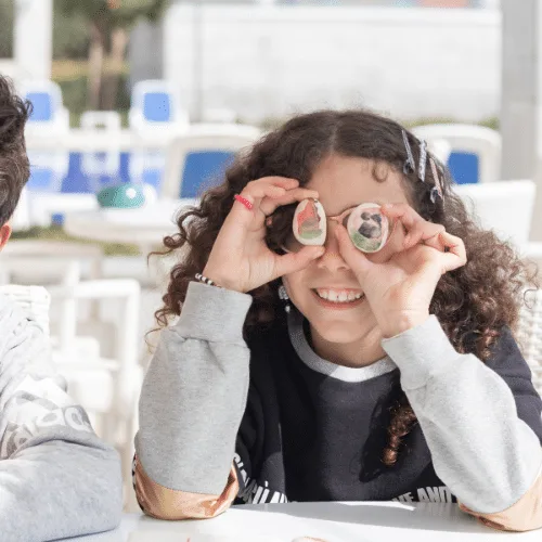 A laughing girl holding two painted stones over her eyes like glasses