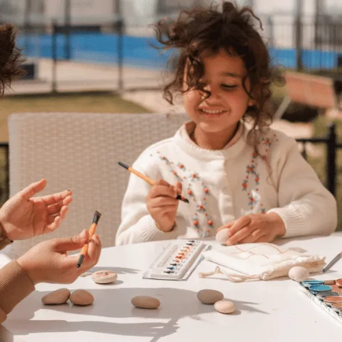 A smiling girl painting stones at an outdoor table