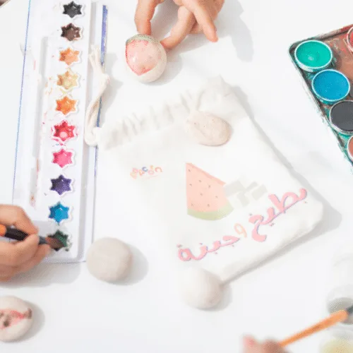 Child painting smooth stones with watercolours next to the Watermelon & Cheese bag