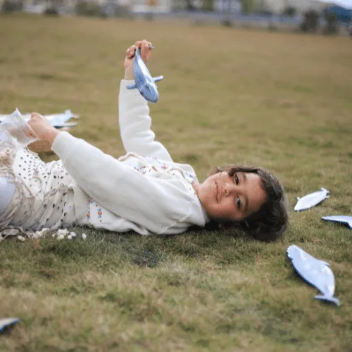 A child lying on the grass playing with a wooden whale