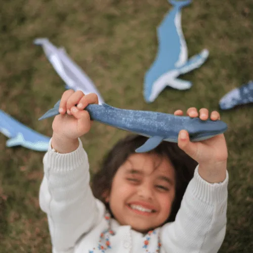 A laughing girl holding a wooden whale above her head