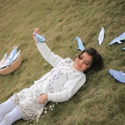 A girl lying on the grass surrounded by Whale's Tummy wooden whales