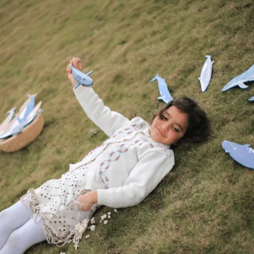 A girl lying on the grass surrounded by Whale's Tummy wooden whales