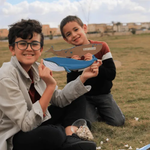Two smiling boys holding a wooden whale outdoors